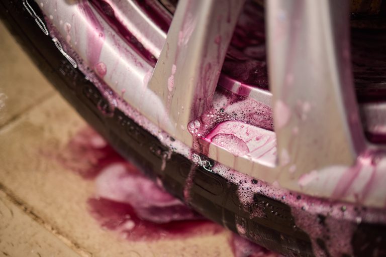 A detailed shot of an automotive tire with water droplets on the rim, showcasing the intricate design of the wheel system and spokes in tints and shades