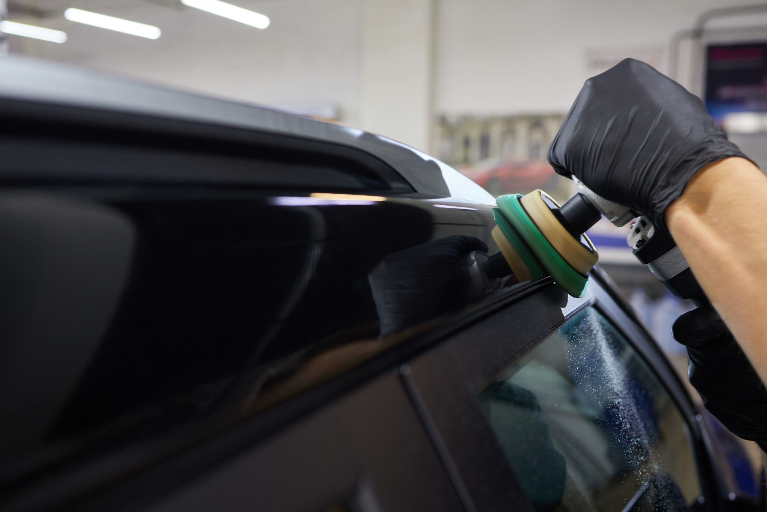 Man with an orbital polisher in car workshop polishing car closeup